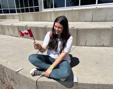 Chica sentada al sol sujetando bandera de Canadá