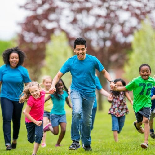 monitores de campamento en el bosque cogiendo de las manos a niños