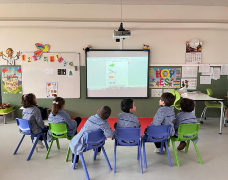 Niños de infantil con mandilones sentados en sillas de colores atendiendo en una clase de inglés