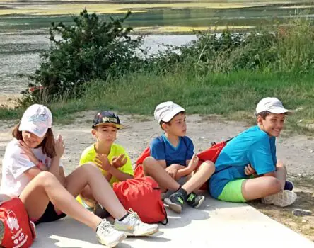 Niños sentados con gorra y al sol en un campamento