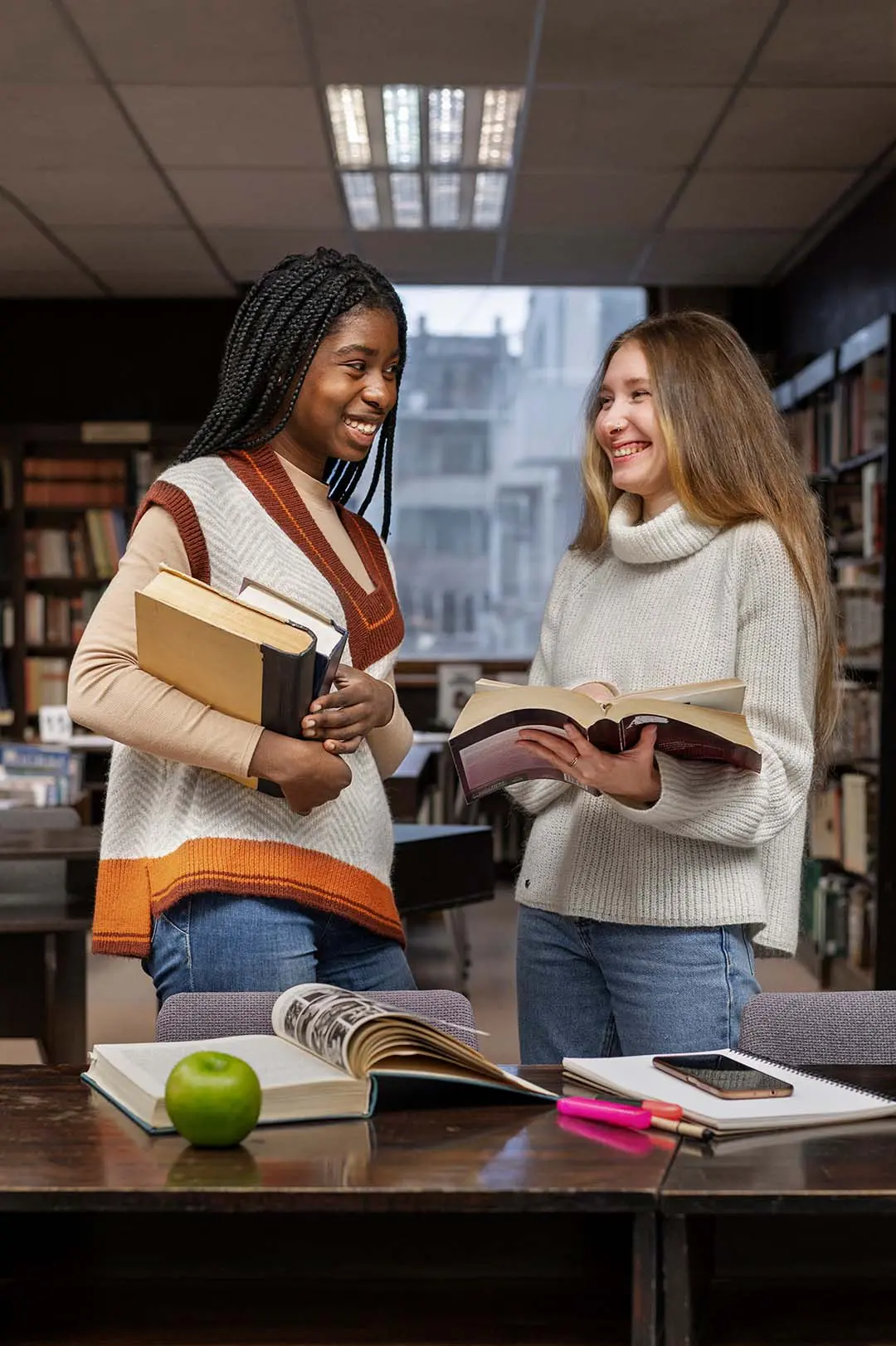 Estudiantes universitarias mirando unos libros y sonriendo en la biblioteca