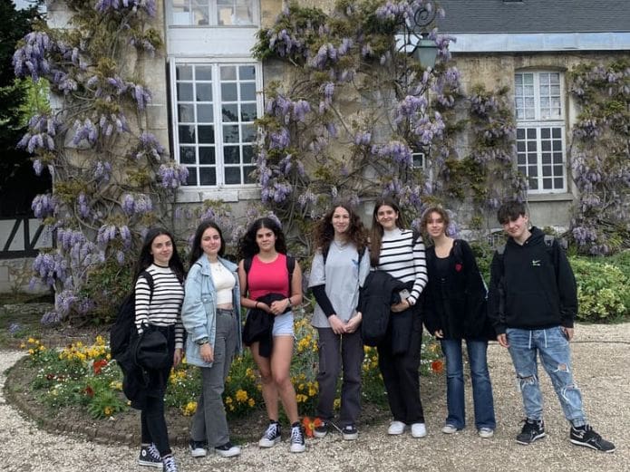 Alumnos posando frente a la fachada de un bonito edificio con flores en Francia