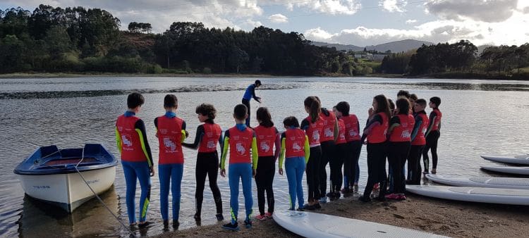 Niños esperando para hacer actividad de paddel surf en la Ría de Foz en su campamento de verano en inglés