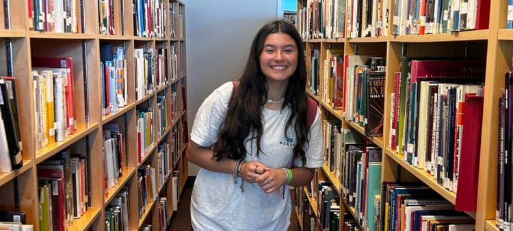 Alumna de Año Académico rodeada de libros en una biblioteca