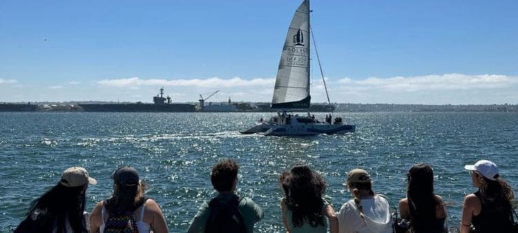 Jovenes mirando a un velero en la costa en verano