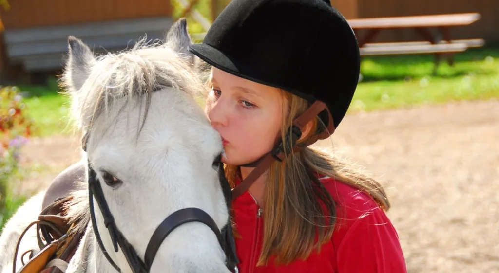 Niña dando un beso a un caballo cuando practica equitación