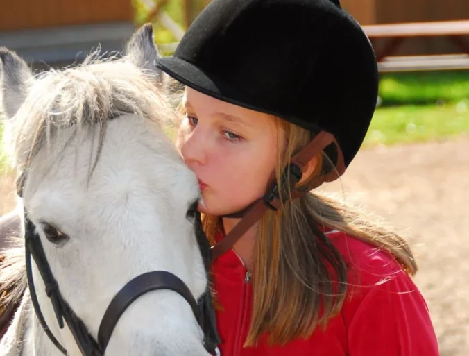 Niña dando un beso a un caballo cuando practica equitación