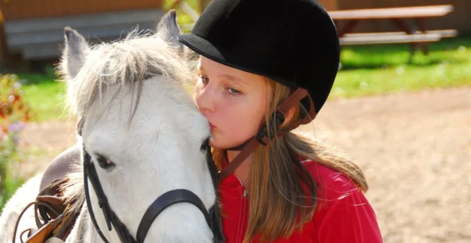 Niña dando un beso a un caballo cuando practica equitación